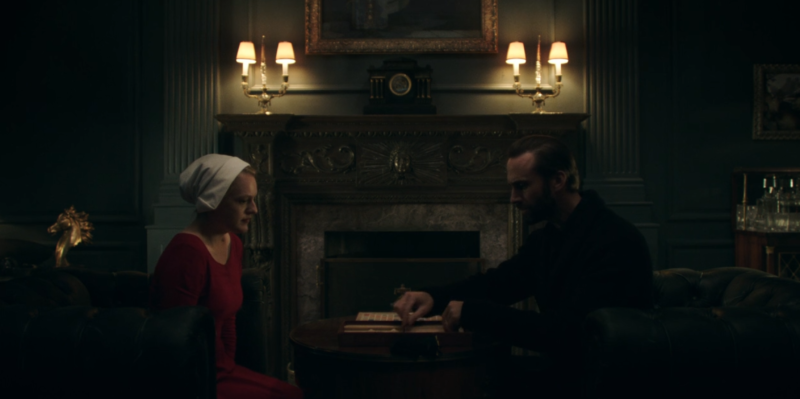 A man and a woman converse in a dimly lit room.